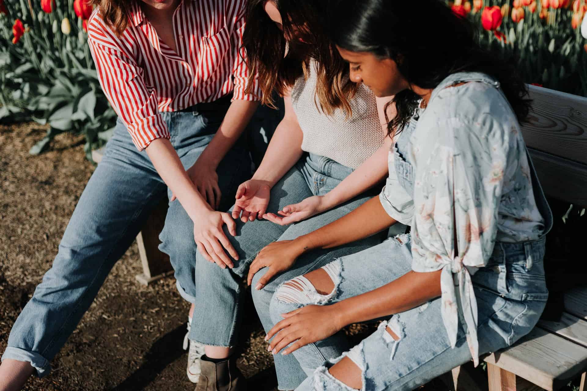 Three women sitting outside on a bench comforting woman in the middle.