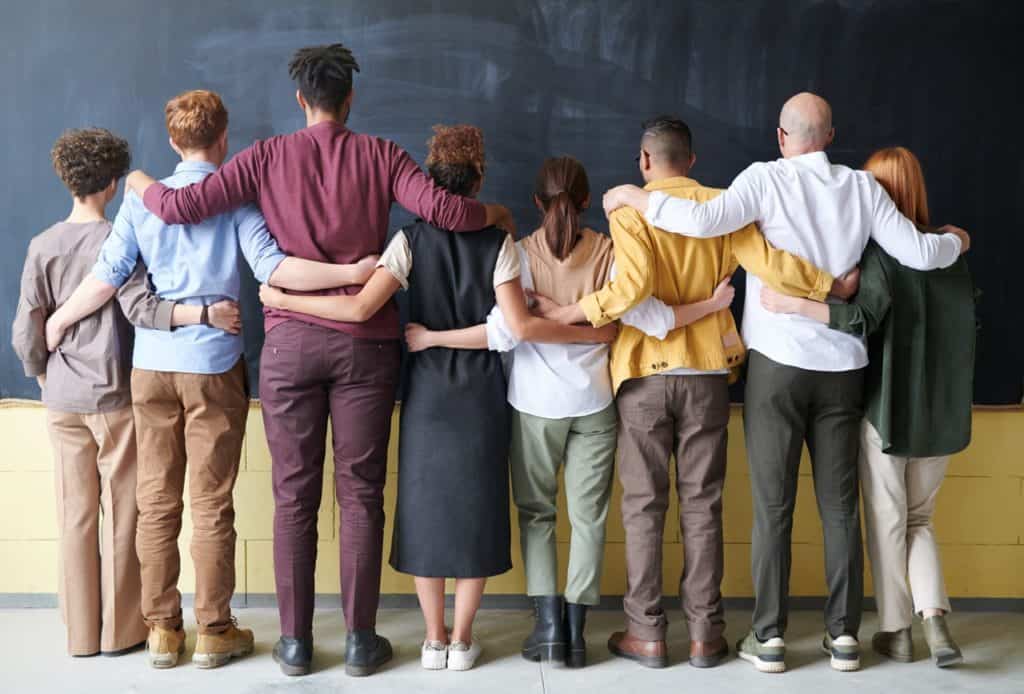 Group of people with back facing us. Arms on each others shoulders.
