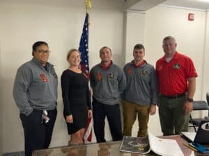 Group of five members of DC Fire standing in front of an American flag wearing red ribbons.