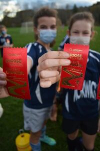 Grade school group of soccer girls holding up red ribbons close to the camera.